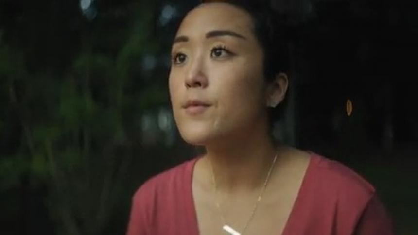 An asian woman is outside and she looks up at the sunrise and smiles