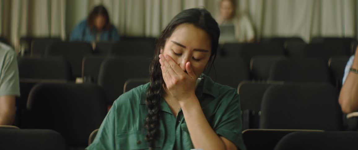 Woman views paper and wipes tears sitting in large room with seating