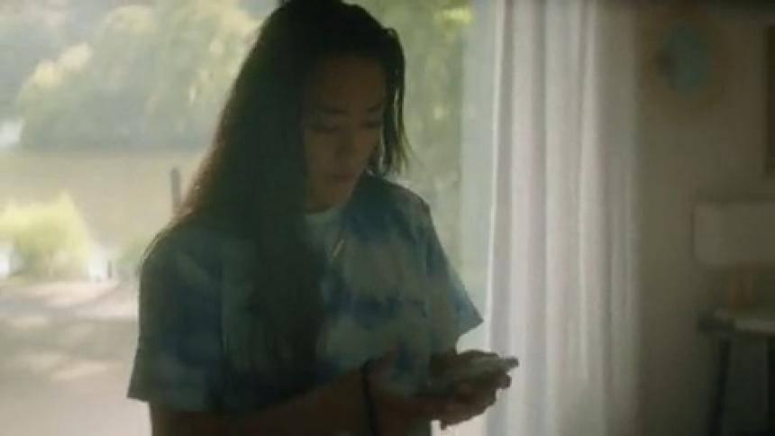 Woman removes a smart phone from her pocket and sits on a bed and looks at the phone while looking sad