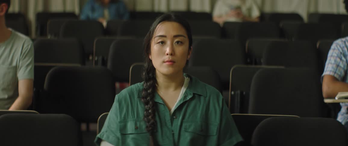 A woman sitting in a lecture hall staring straight ahead as others talk and read