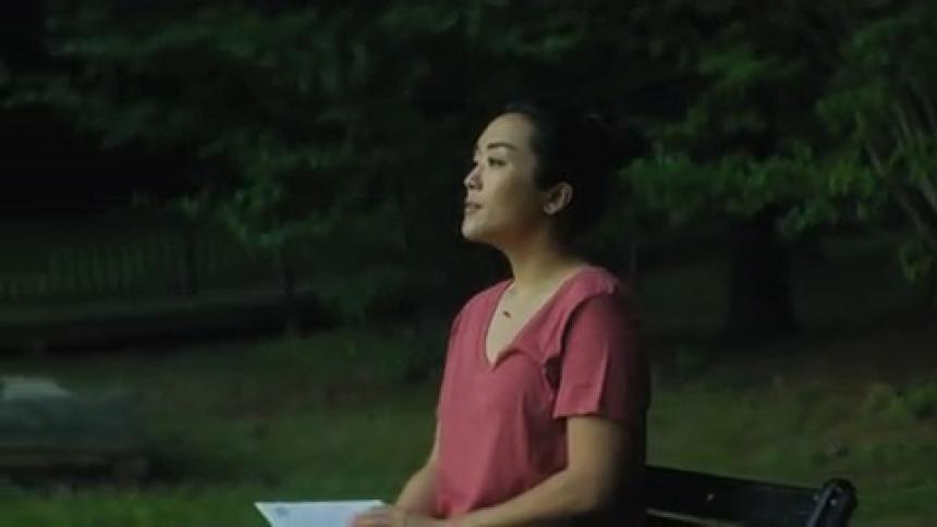 A woman is sitting outside on a park bench with a book in her lap and she gets up and walks away