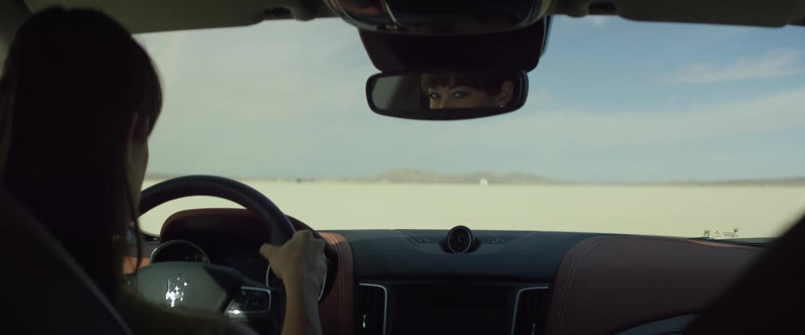 Woman with brown hair sits in car looking across desert