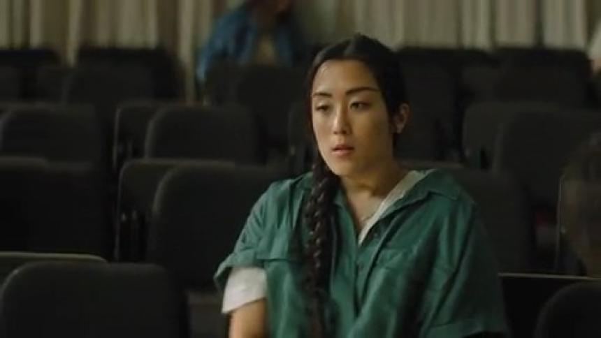 Upset woman sits alone in seat in classroom as other nearby people talk amongst themselves