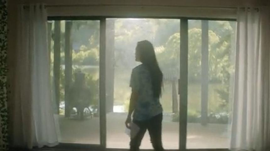 A woman walks to a mirror beside a glass door