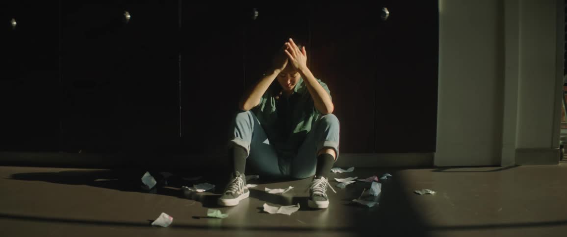 A sad student drops paper on the floor near the locker