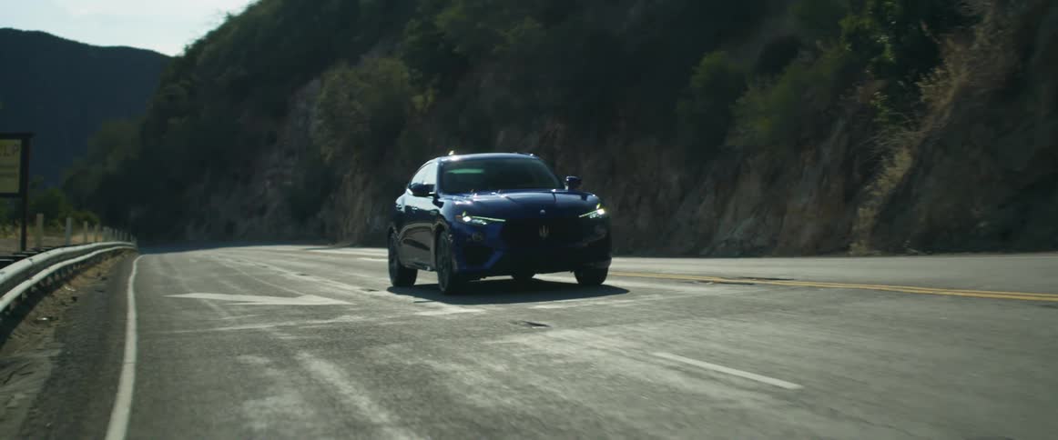 A dark blue automobile is traveling on a road along the side of a mountain