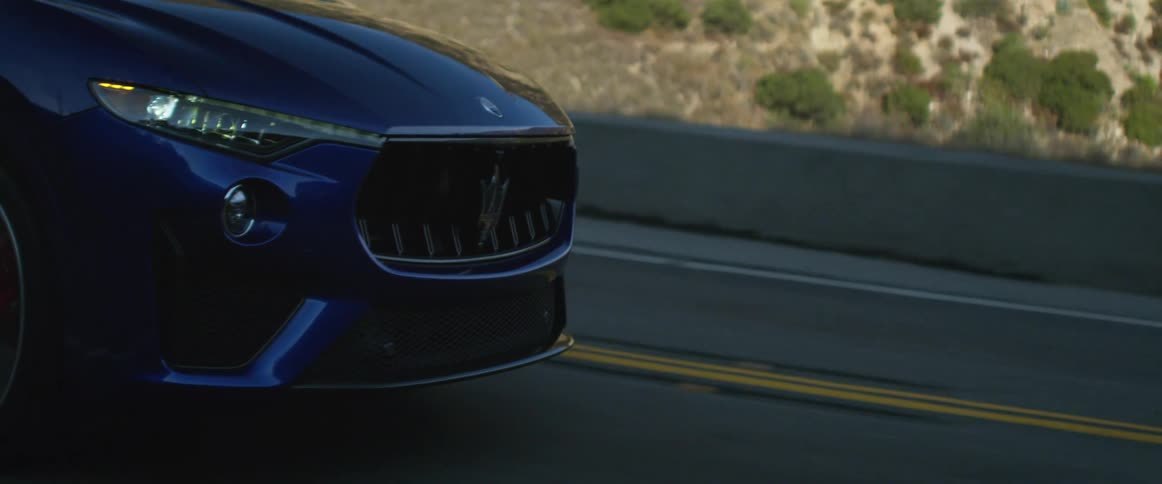 A dark blue luxury vehicle driving on a paved road in the daytime