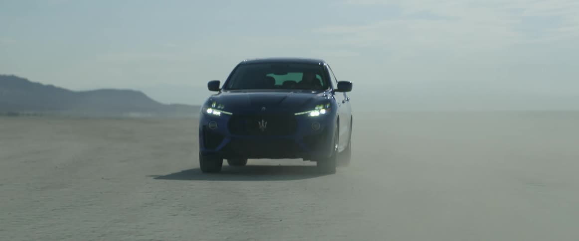 A car is driving across the salt flats near a mountain range