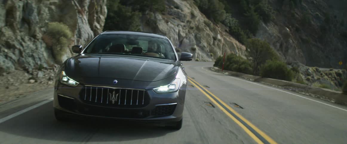 A man drives a luxury car along a mountain pass during the day