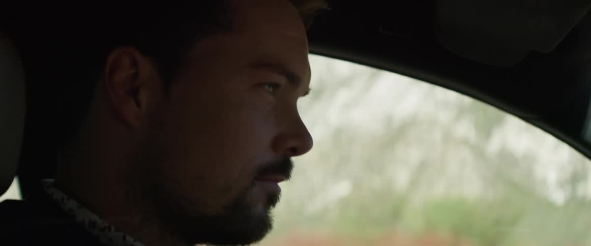Man with a beard and mustache smiles as he travels in a vehicle past the mountains