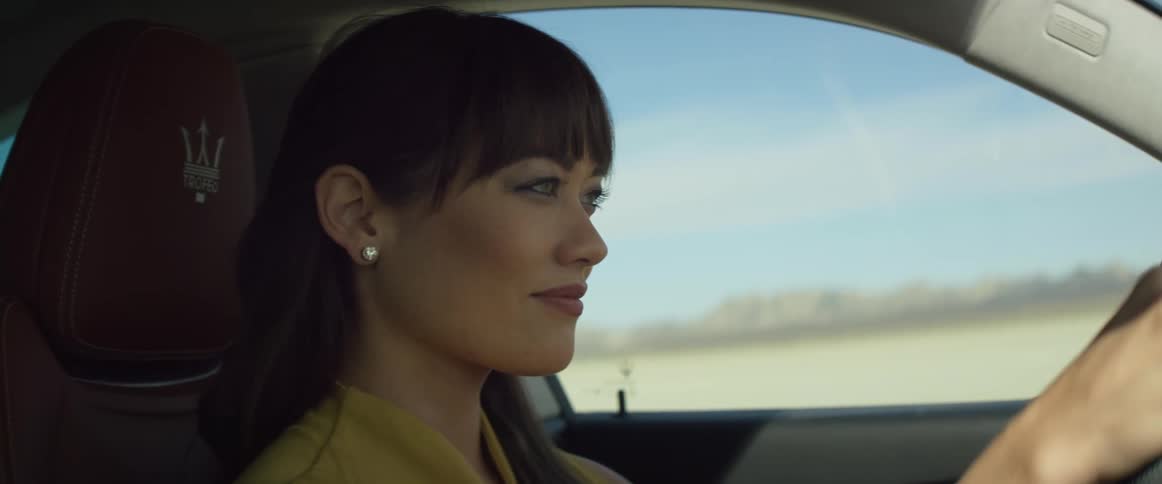 A woman is driving an automobile with a grin on her face and she turns to look behind her and smiles