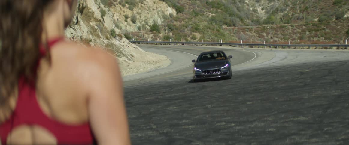 Woman in a pony tail stands near the highway as a car pulls up in front of her