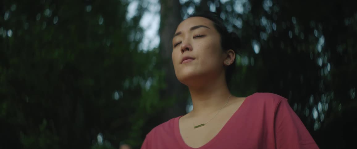 Woman stands in the forest with her eyes closed then opens her eyes and breathes deeply and smiles