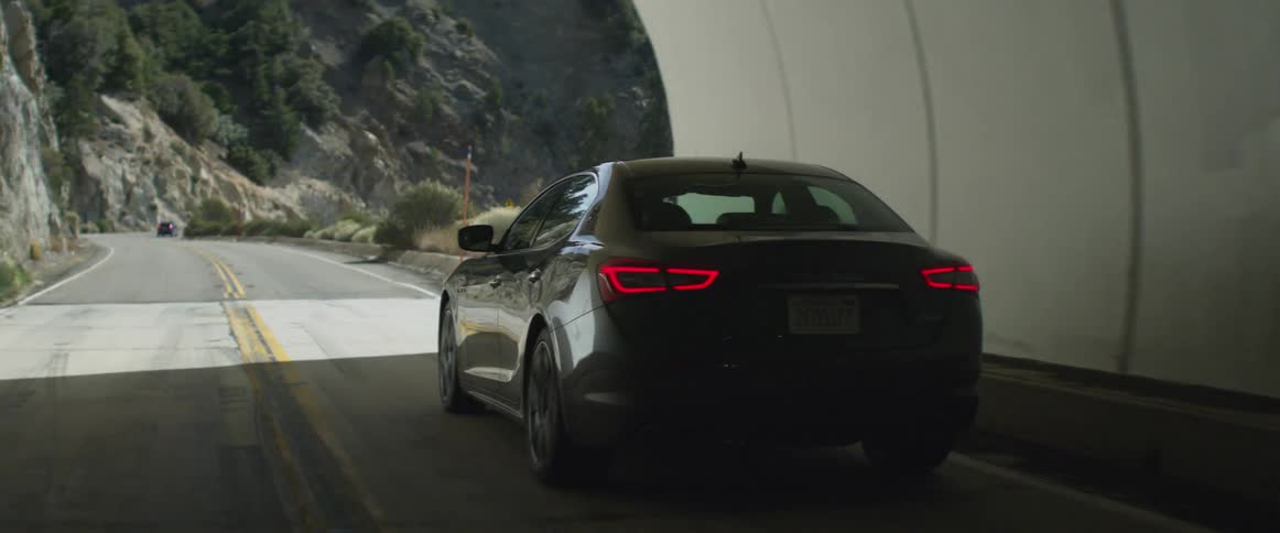 Gray sports car drives on mountain highway through tunnel