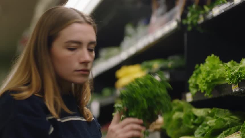 A woman reaches for a bunch of parsley and smells the aroma before placing in her cart