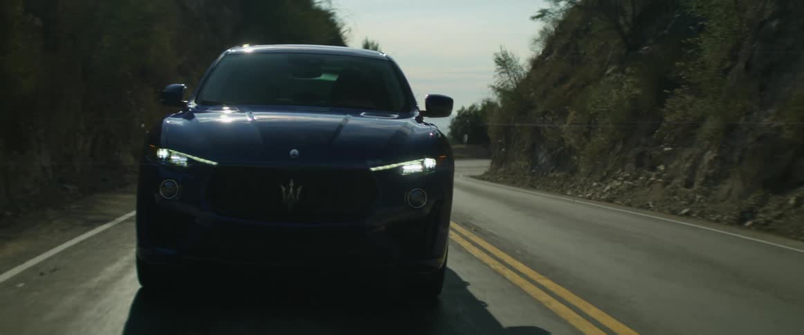A car is driving through mountains with just enough room for the road