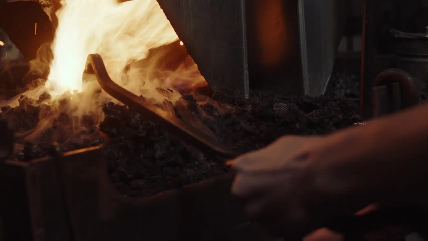 A man uses a fire poker to break up rocks in a kiln