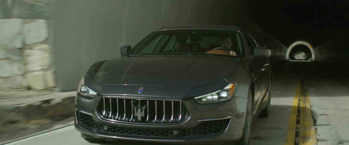 A car drives through a dark mountain tunnel out onto the sunny highway
