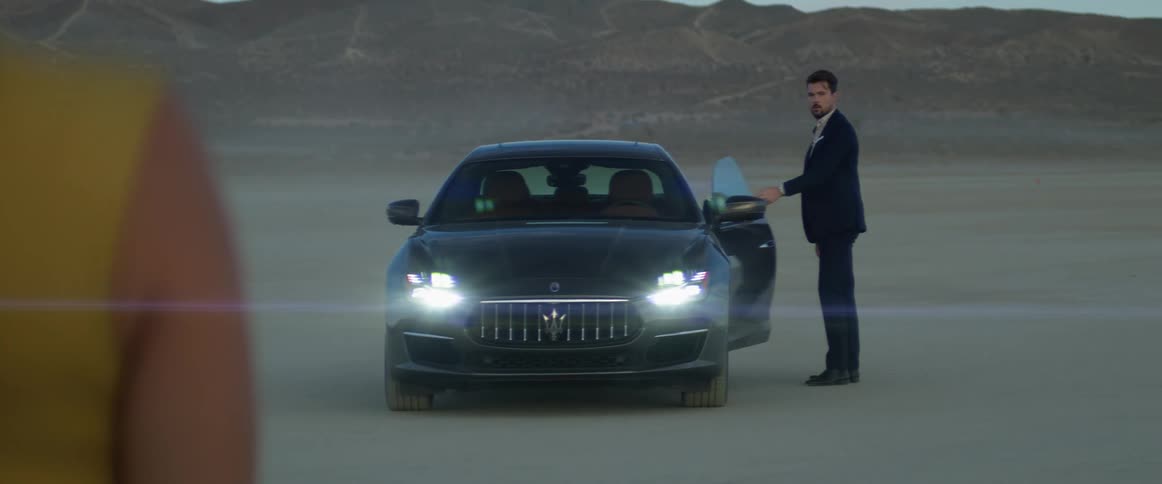 A woman stands and waits as a man gets out of a grey car and walks toward her