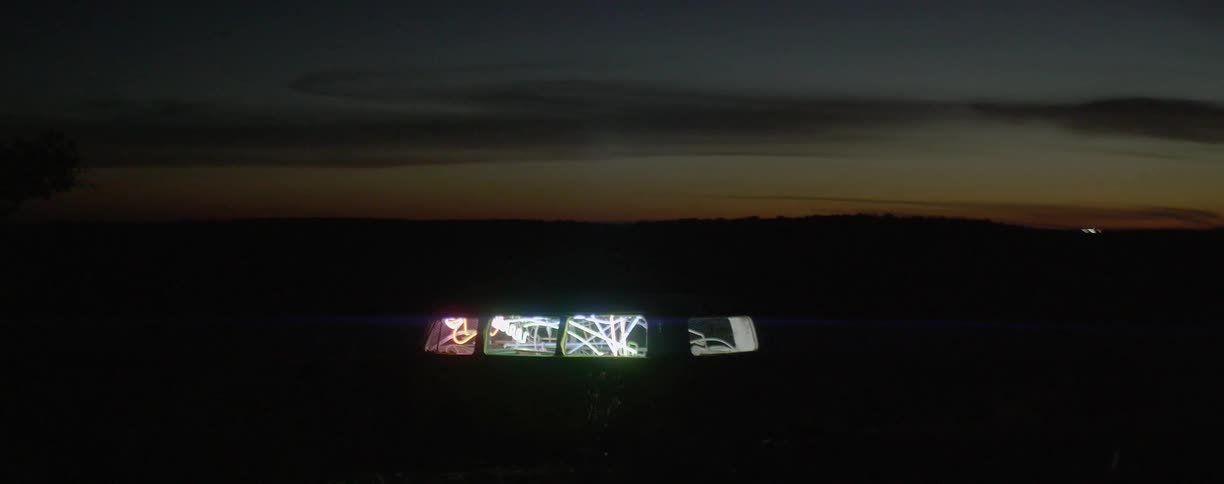 A car passes on the road behind a van with lights inside