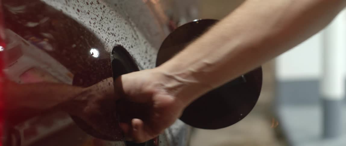 A man unscrews and removes the fuel cap from a vehicle outdoors during the day