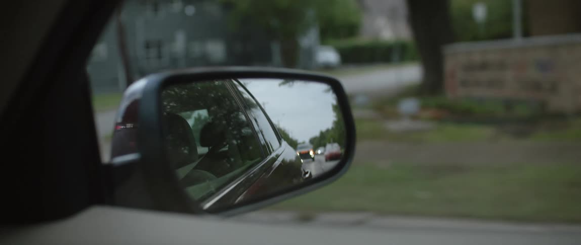 Looking out the window automobiles can be seen traveling behind this car through the side view mirror