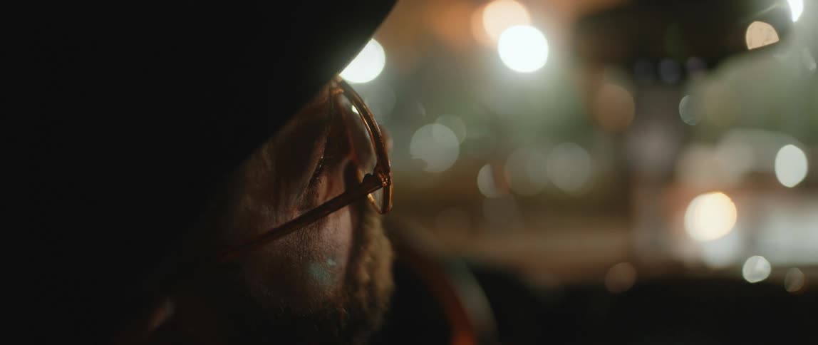 An elderly man sits in his car and looks out the window at night