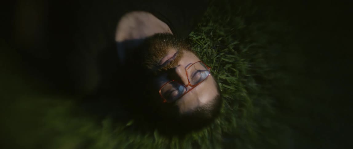 Light beam glints of eyeglasses of man lying with eyes closed on grass at night