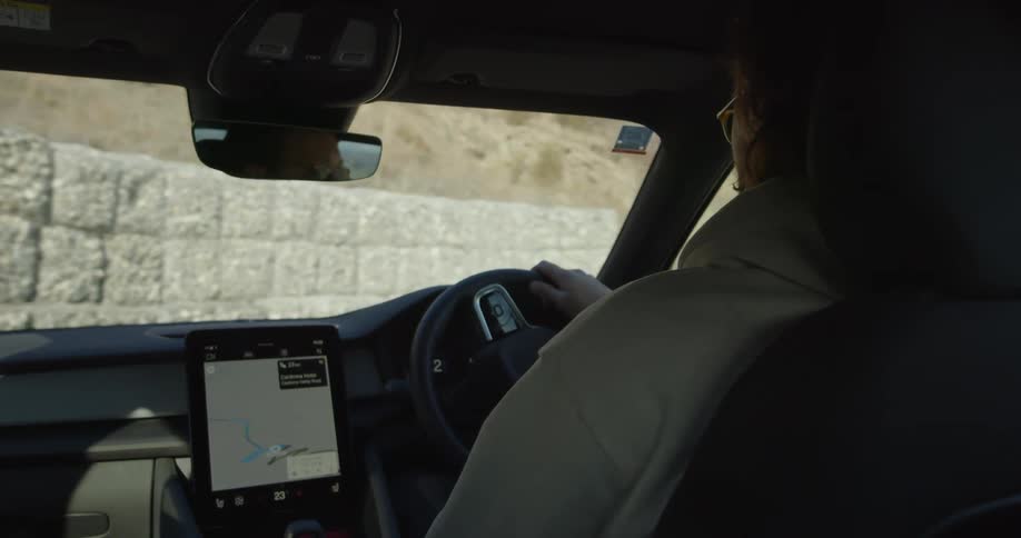 A man turns his car onto a mountain road with a snow dusted ridge in the distance