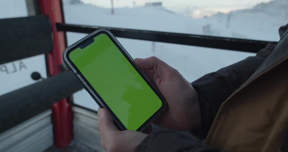 A person looks at the screen of their smartphone while riding a ski lift up a snowy mountain