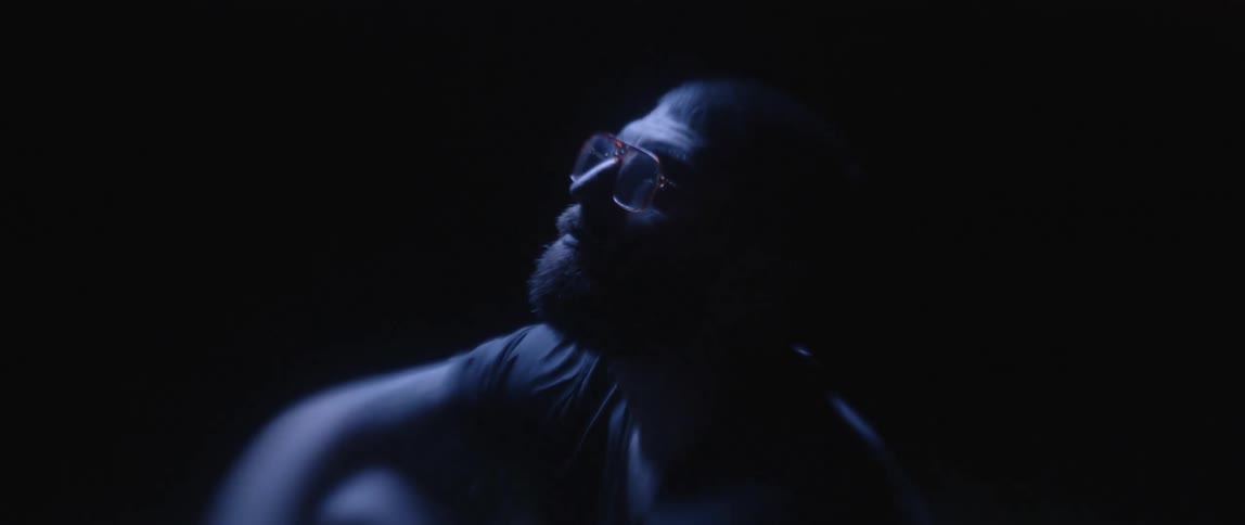 A man sitting in the dark lifts his head and looks up