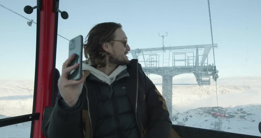Man riding overhead cable car talk via smartphone and shows view of the snow covered mountains
