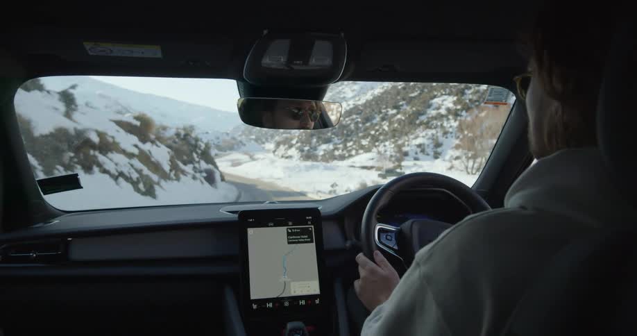 A man drives a car along a road through a snowy valley while using a tablet as a gps