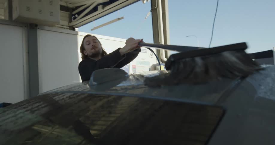 A man washes his car manually at a car wash