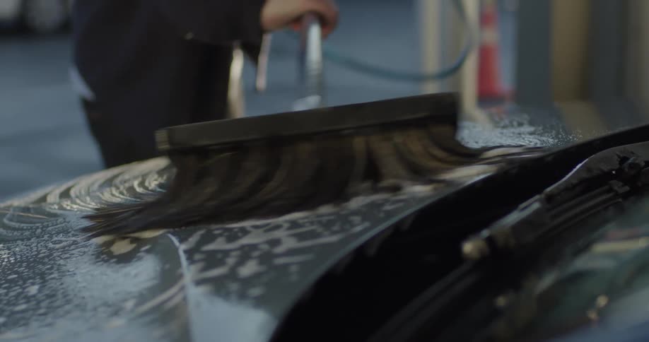 A man is outside washing his car with a soapy brush