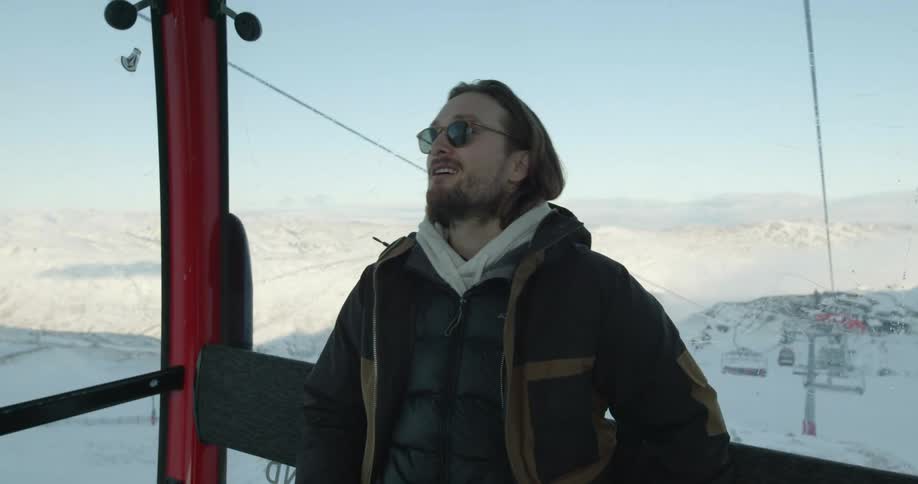 A man riding in a ski gondola smiles as he tucks his phone into his jacket