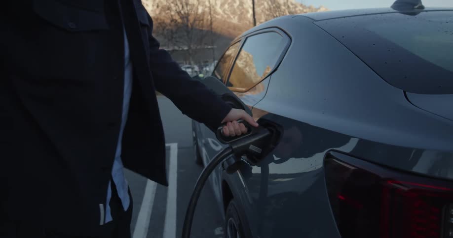 A man charges his electric car in a business parking lot