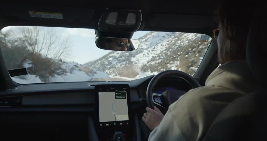 A woman is driving an automobile on a snow covered mountain road and there is a gps on the dashboard