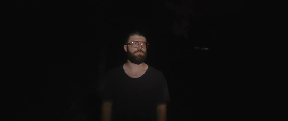 A man stands outside and looks ahead as lights shine on him