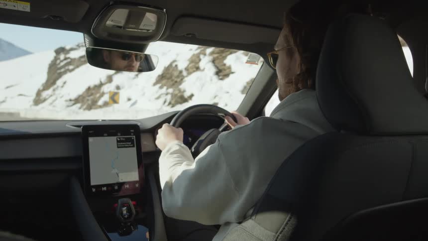 Man wearing eyeglasses drives along road near snow covered mountain slope