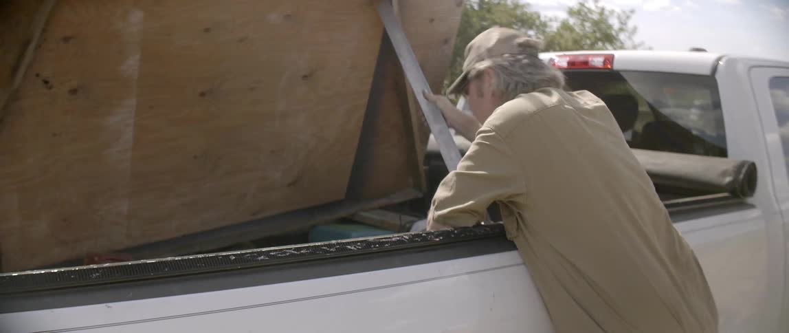 A man stoops open a board of wood in the back of his truck