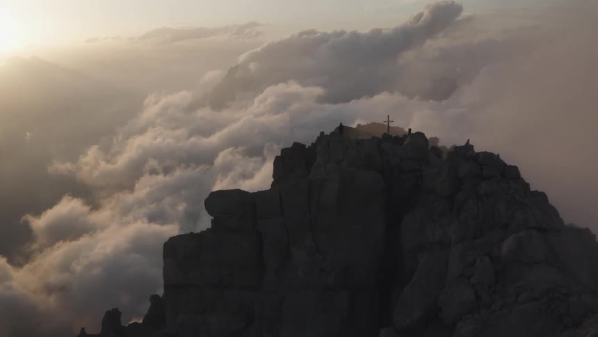 A man stands next to a cross on a large rocky cliff