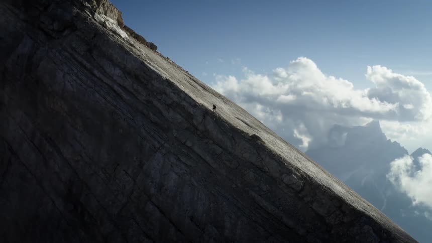A person is climbing up a mountain slope under a cloudy sky
