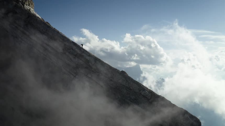 Mountain climber climbs up the slope of a mountain on a sunny day