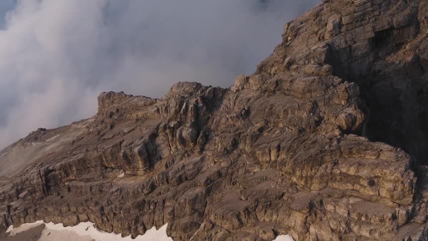 A rocky mountain ridge among the clouds with snow on the ledge and peaks high in the sky