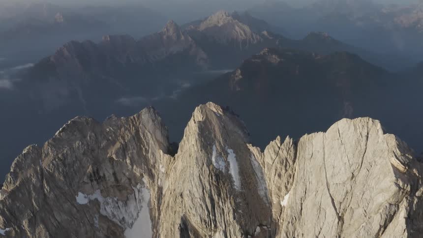 Snow dusts side of craggy rocky mountain bordering fog covered mountain range