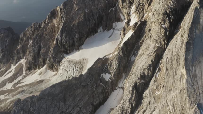 The sun shines on a mountainside with snow along the slope