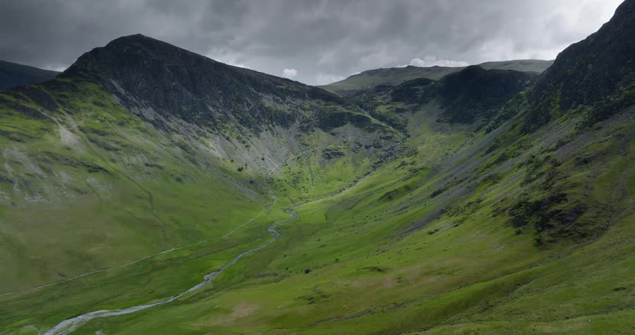 A mountain valley covered in vegetation between mountain ridges of black stone on a cloudy day