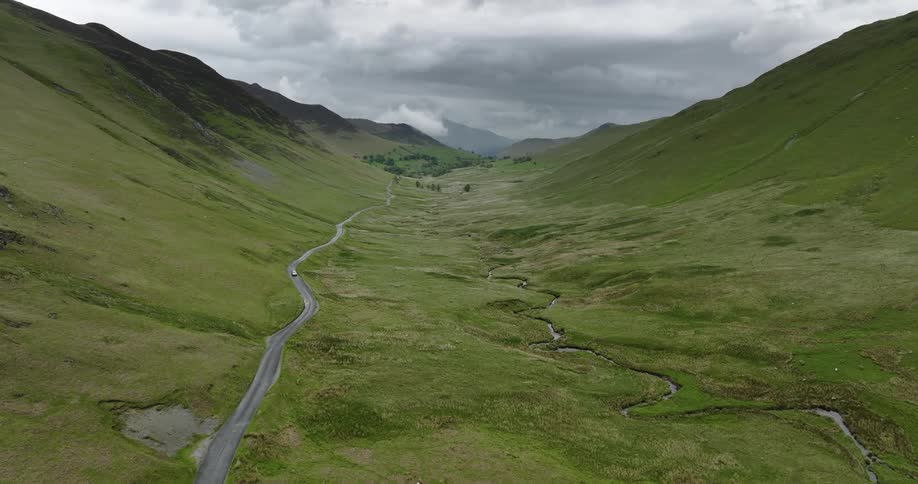 An aerial view of a car driving on a road next to a river in a valley