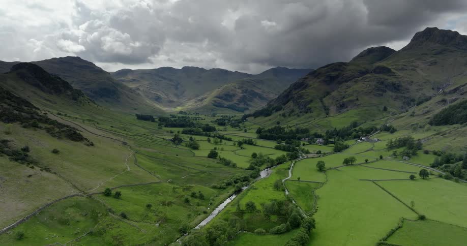 Lush green grass fields in a valley with a winding stream